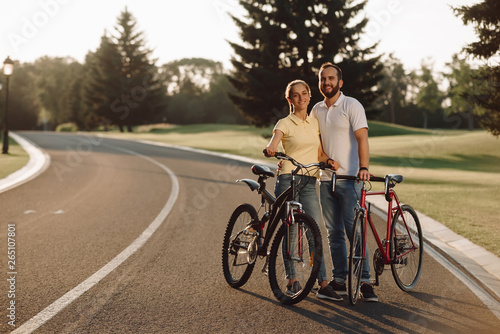 Happy couple posing with bicycles on the road. Smiling cyclists resting on the road. Summer weekend together.