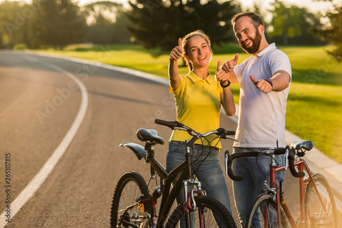 Joyful couple of cyclists gesturing thumbs up. Happy smiling people giving thumbs up sign outdoors. Summer active rest.