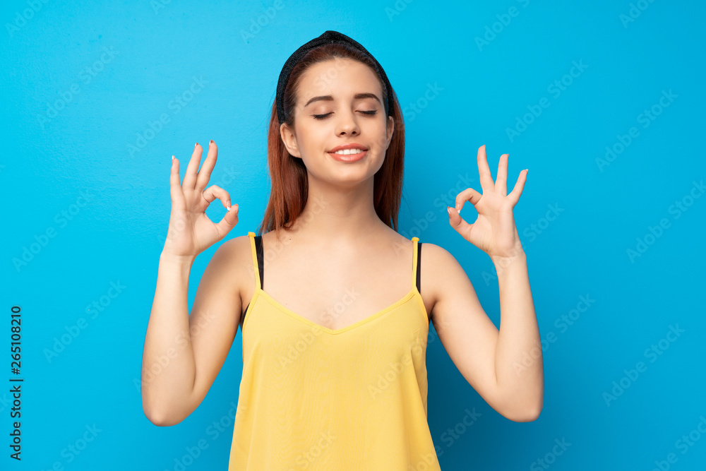 Young redhead woman over blue background in zen pose Young redhead woman over blue background in zen pose