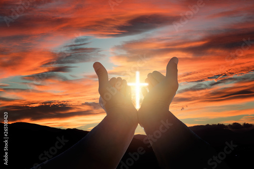 Christian man with open hands, sunshine in the shape of a crucifix and dramatic sky.