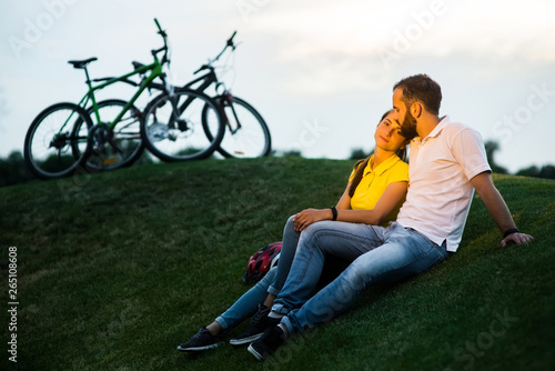 Young couple on meadow at sunset. Cute couple of students in love resting on green hill. Romantic date with bikes outdoors.