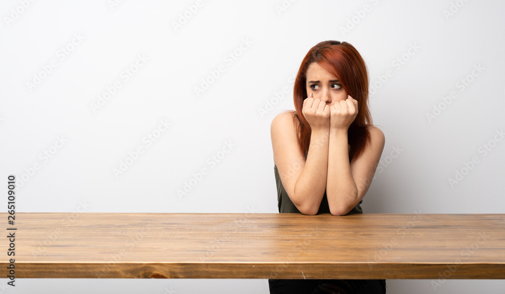 Young redhead woman at desk nervous and scared putting hands to mouth Young redhead woman at desk nervous and scared putting hands to mouth