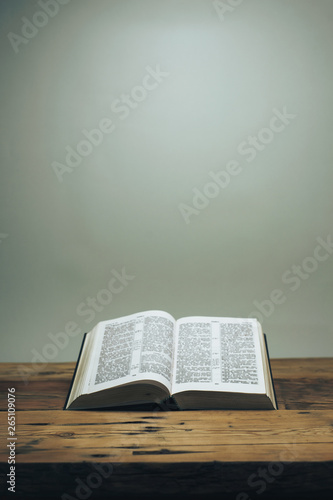Open Holy Bible on a old oak wooden table.  Grey wall background..