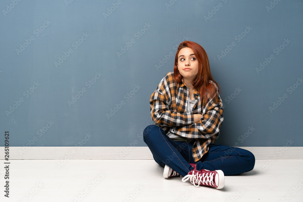 Young redhead woman sitting on floor making doubts gesture while lifting the shoulders Young redhead woman sitting on floor making doubts gesture while lifting the shoulders
