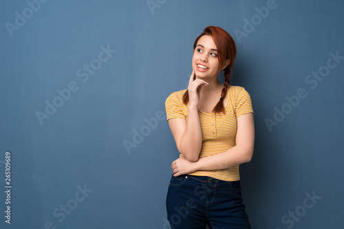 Young redhead woman over blue background thinking an idea while looking up © luismolinero