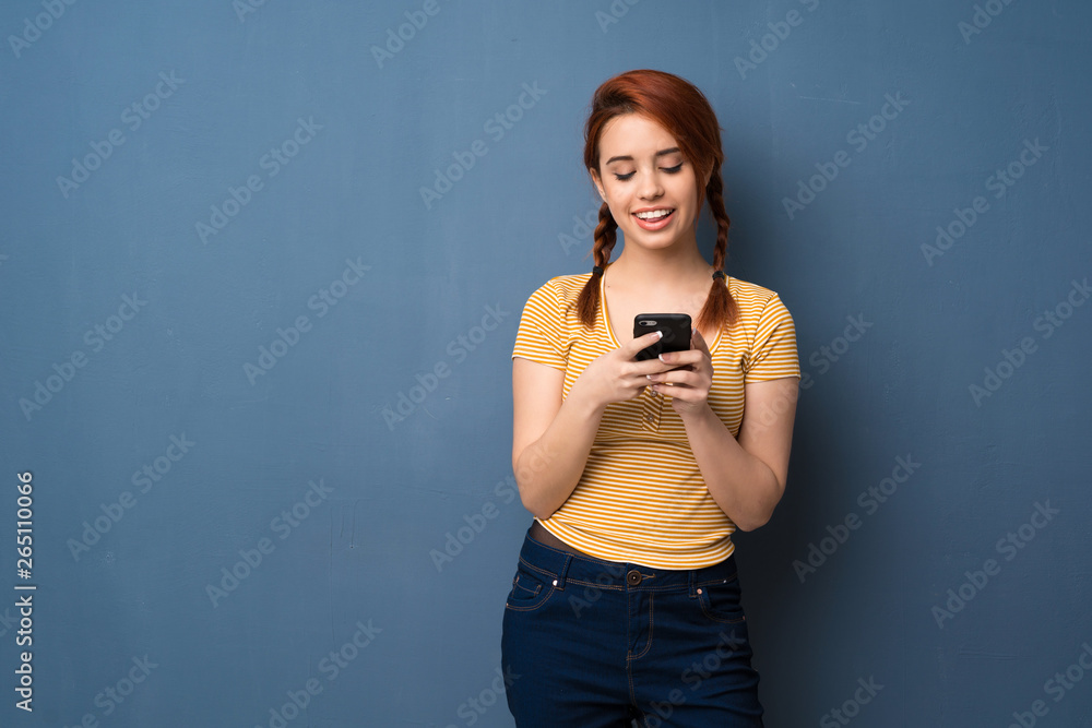 Young redhead woman over blue background sending a message with the mobile Young redhead woman over blue background sending a message with the mobile
