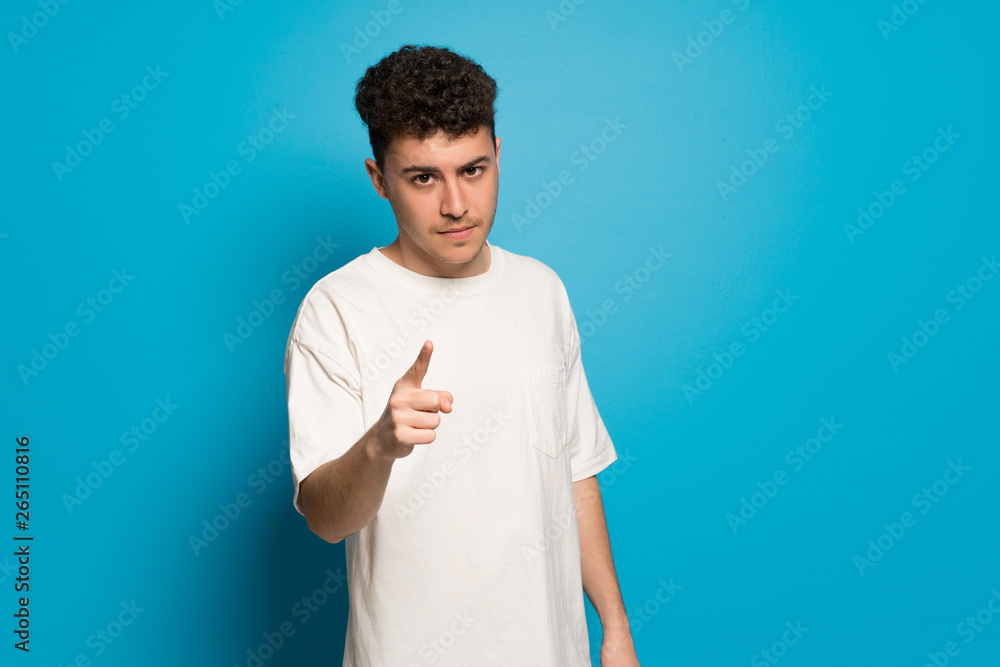 Young man over blue background serious and pointing to the front Young man over blue background serious and pointing to the front