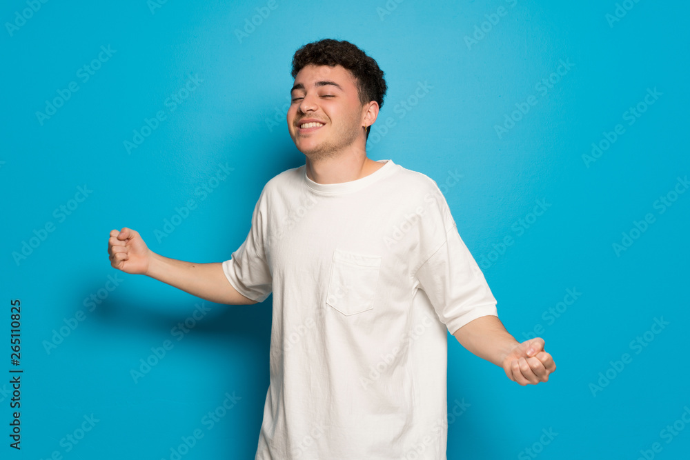 Young man over blue background enjoy dancing while listening to music at a party Young man over blue background enjoy dancing while listening to music at a party