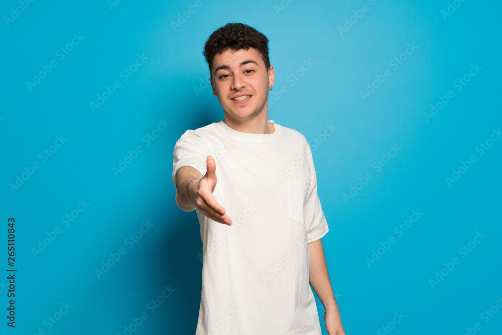 Young man over blue background shaking hands for closing a good deal Young man over blue background shaking hands for closing a good deal