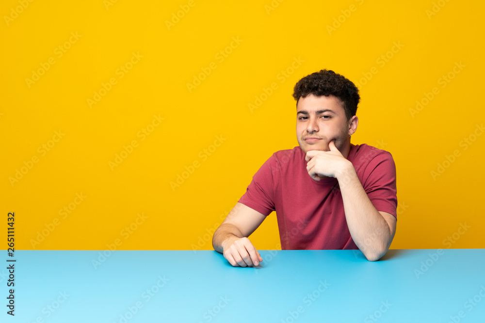 Young man with colorful wall and table thinking Young man with colorful wall and table thinking