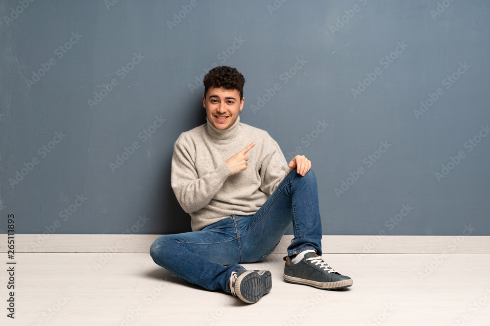 Young man sitting on the floor pointing to the side to present a product Young man sitting on the floor pointing to the side to present a product