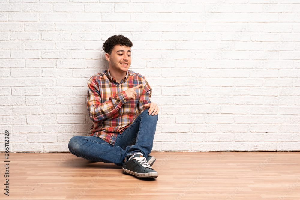 Young man sitting on the floor pointing to the side to present a product Young man sitting on the floor pointing to the side to present a product