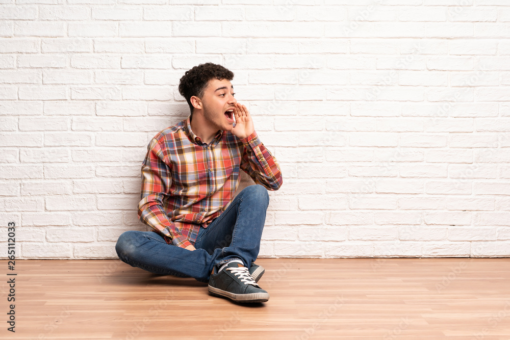 Young man sitting on the floor shouting with mouth wide open to the lateral Young man sitting on the floor shouting with mouth wide open to the lateral
