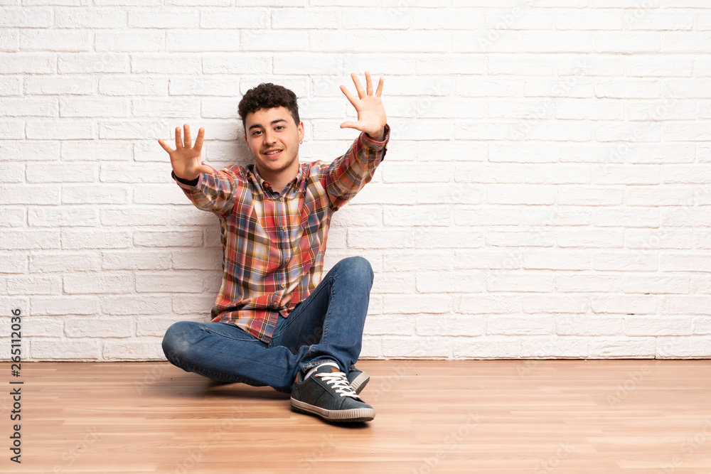 Young man sitting on the floor counting ten with fingers Young man sitting on the floor counting ten with fingers