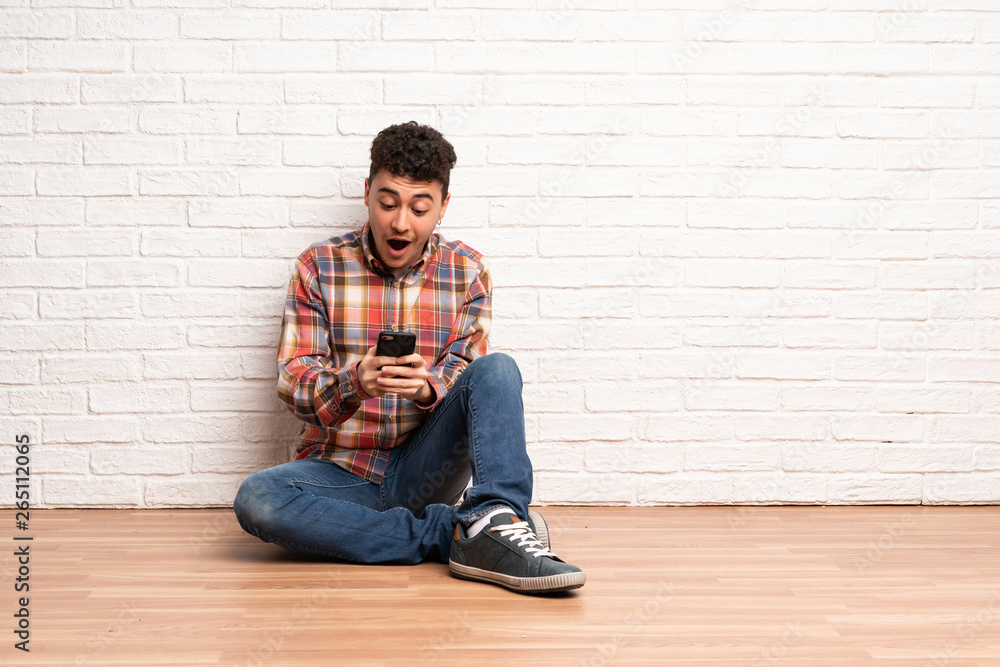 Young man sitting on the floor surprised and sending a message Young man sitting on the floor surprised and sending a message