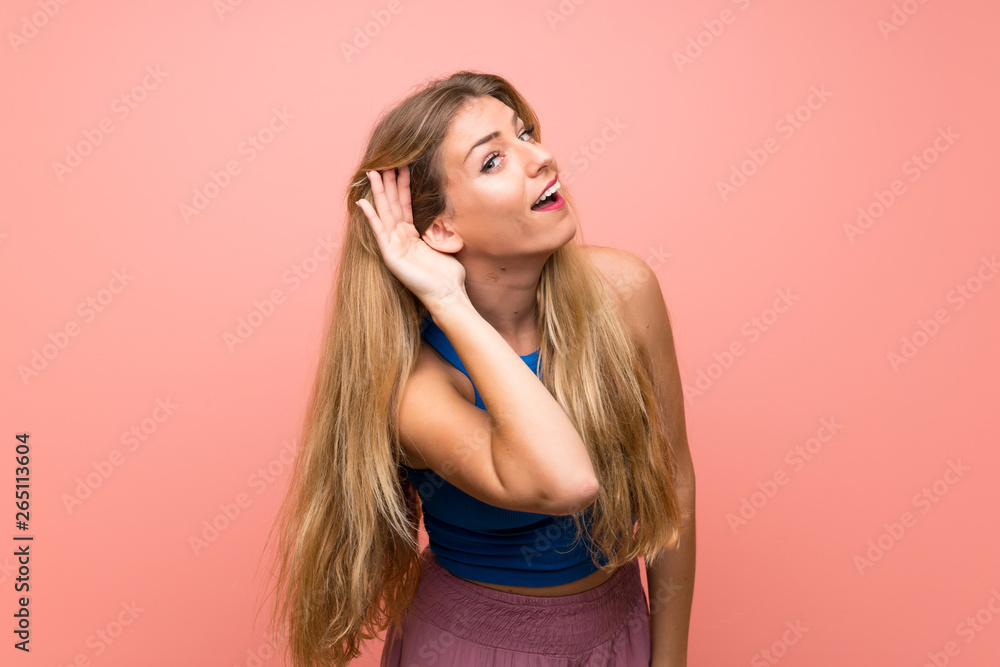 Young blonde woman over isolated pink background listening to something by putting hand on the ear - obrazy, fototapety, plakaty 