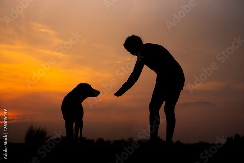 Silhouette women playing with dog at sunset - Image © patcharee11