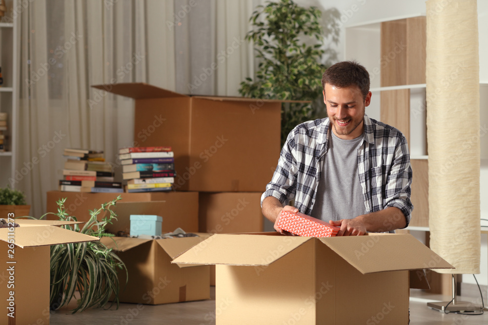 Happy man moving home unboxing belongings in the night