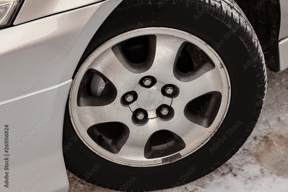 Chrome-plated cast aluminum wheel on the car with a black rubber tire, five holes for mounting bolts and six spokes through which the brake disk is visible, in the wing arch
