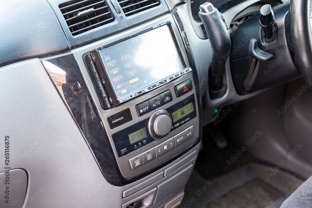 The central control console on the panel inside the car close-up with climate control and audio system and a hole for the CD and emergency button in gray and black. Auto service industry. Comfort.