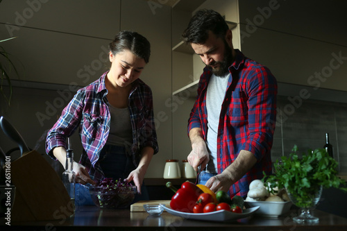 Beautiful young couple in kitchen at home while cooking healthy food. Husband cut cabbage. Wife mix salad. Scene from family life.