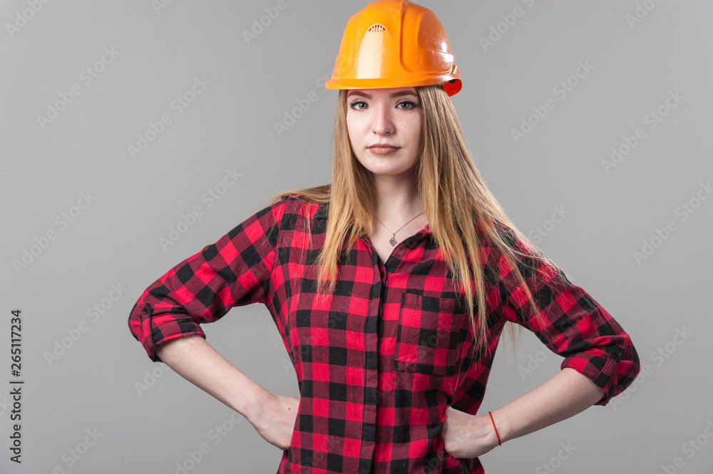 Portrait of a young attractive woman with blond hair in orange helmet on a neutral gray background. Portrait of a young attractive woman with blond hair in orange helmet on a neutral gray background.