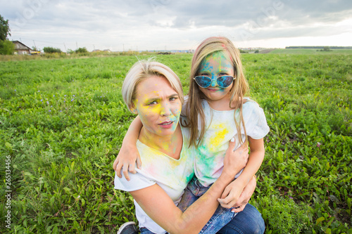 Happiness  Holi festival and holidays concept - Mother and her daughter covered with color powder smiling over nature background