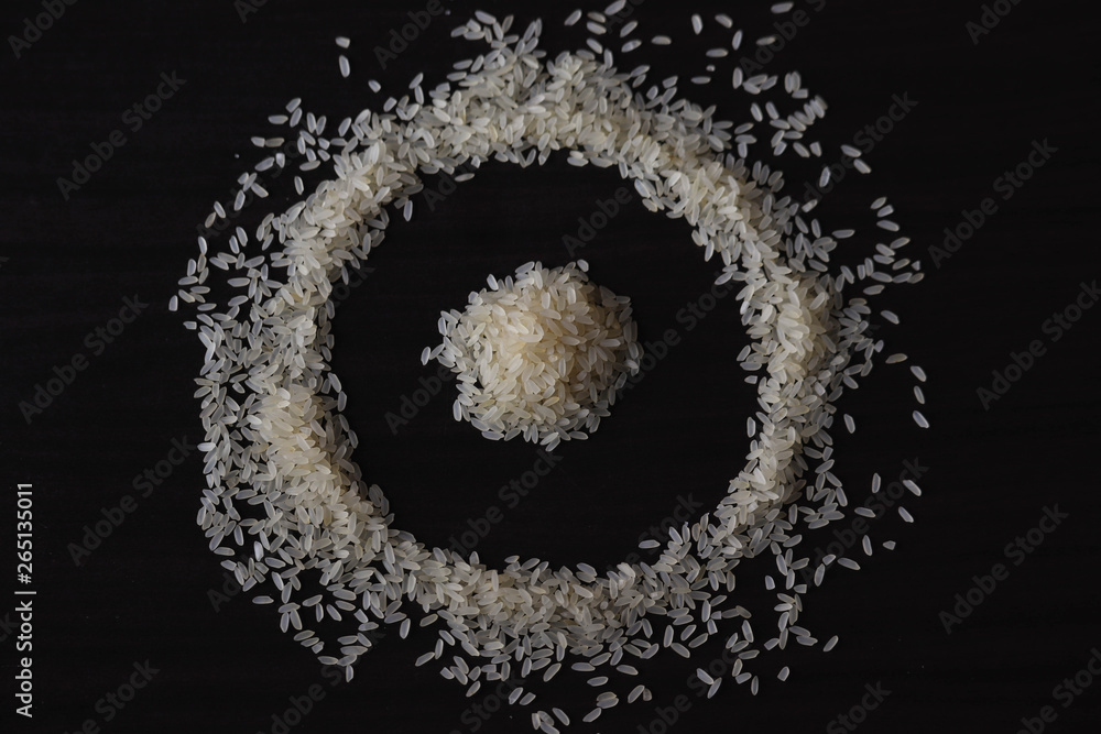 some amount of raw rice laying o the table ,creating a design.background is dark wooden table some amount of raw rice laying o the table ,creating a design.background is dark wooden table