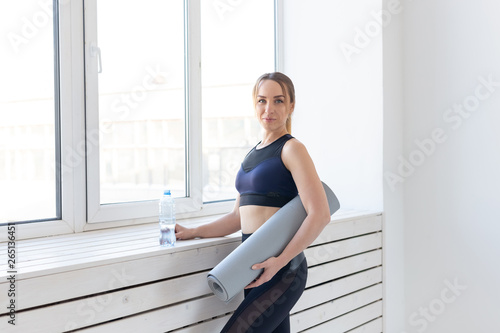 Yoga, healthy and sport concept - Young fit woman holding grey mat and bottle of water