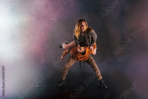 Fototapeta Naklejka Na Ścianę i Meble -  Strong male dancer and an elegant female dancer perform an exotic and unique dance moves in front of a black background while wearing urban clothes.