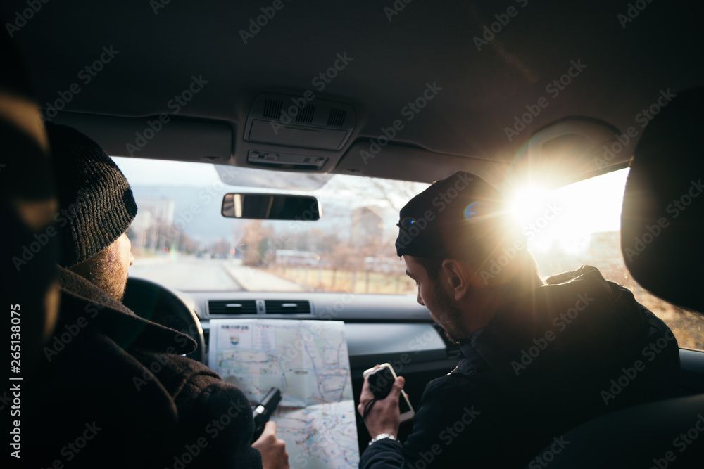 Criminals sitting at sunset in a car, looking at the city map and planning their next move.