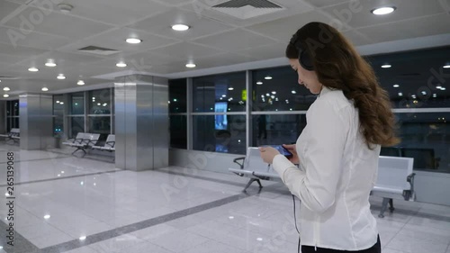 Woman watch movie on smartphone while walking at airport passage, half length tracking shot. Modern interior of international terminal sterile area, passenger spend time with film on mobile device photo