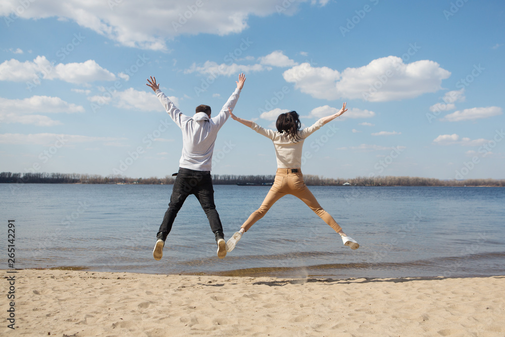 Obraz premium stylish young couple spends time together on the beach. happy boyfriend and girlfriend jump on the river bank