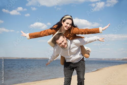 Happy man carrying his girlfriend on back like plane outdoors in sunny day