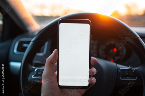Man holds a smartphone with mockup in the car on sunset background