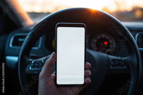 Man holds a smartphone with mockup in the car on sunset background © Lalandrew