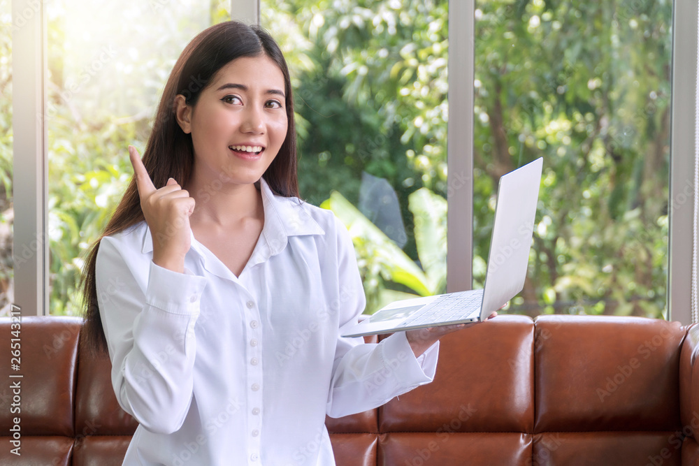 Freelancer young woman with long dark hair holding laptop and pointing upwards while sitting brown sofa getting new idea. Business women working online with silver computer at home. lifestyle concept. Freelancer young woman with long dark hair holding laptop and pointing upwards while sitting brown sofa getting new idea. Business women working online with silver computer at home. lifestyle concept.