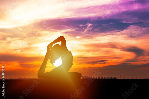 Silhouette of healthy young woman practicing yoga meditation during on background city with sky and sunset.