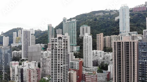 Tall apartment buildings at Mid-Levels, Hong Kong. Typical residential area of HK island, green mountain seen on background. Narrow and high towers stick up, dense build in small area photo