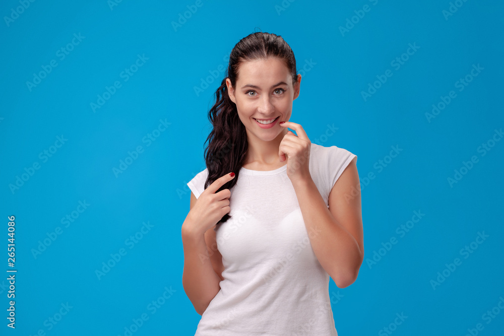 Studio portrait of a young beautiful woman in a white t-shirt against a blue wall background. People sincere emotions. Studio portrait of a young beautiful woman in a white t-shirt against a blue wall background. People sincere emotions.