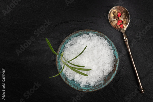 Gourmet spices. Rosemary infused sea salt and a spoon with peppercorns, shot from the top on a black background with a place for text