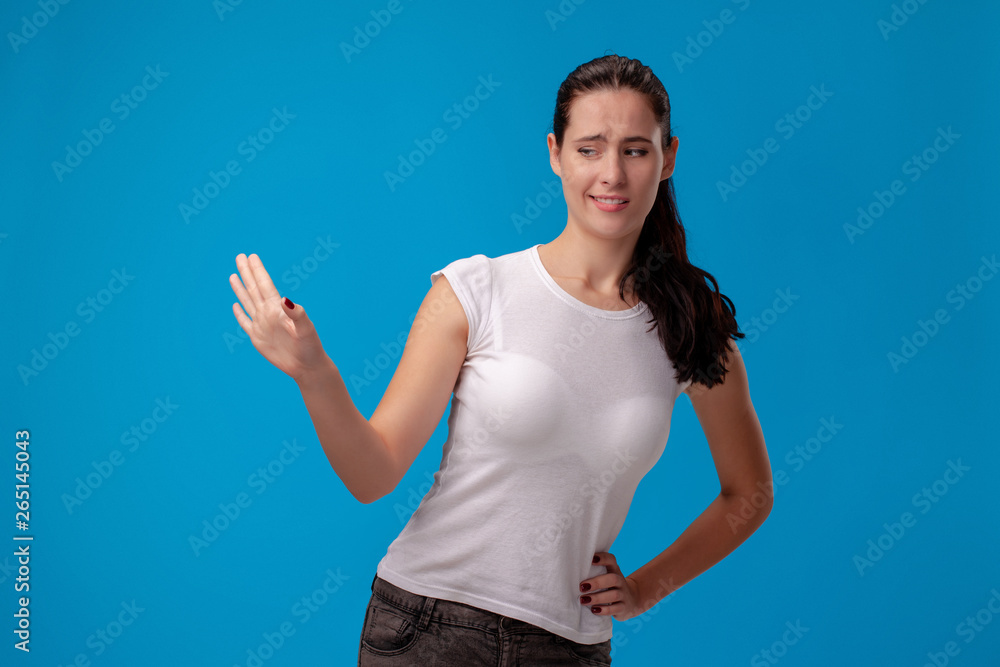 Fototapeta premium Studio portrait of a young beautiful woman in a white t-shirt against a blue wall background. People sincere emotions.
