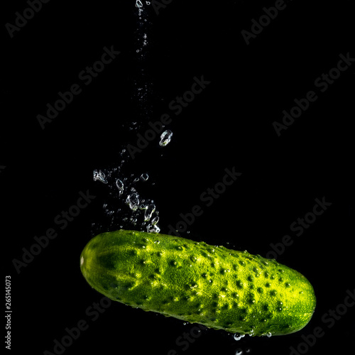 green juicy cucumber falls into the water with splashes