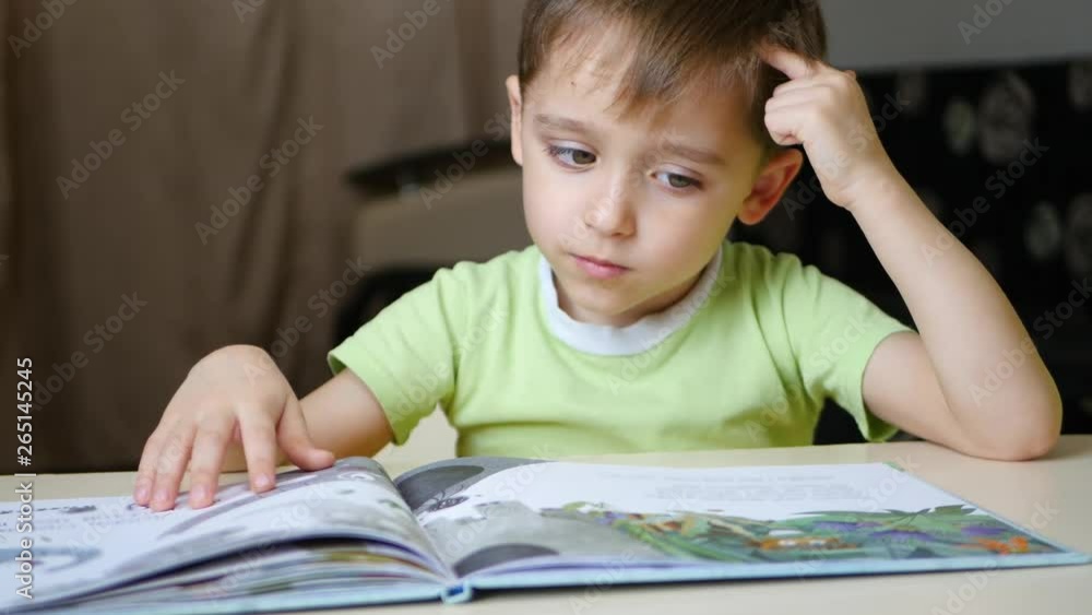 The child thoughtfully reads a book while sitting at the table at home The child thoughtfully reads a book while sitting at the table at home