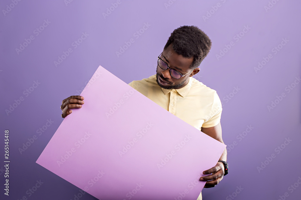 Picture of young african american man holding blank board on violet background Picture of young african american man holding blank board on violet background