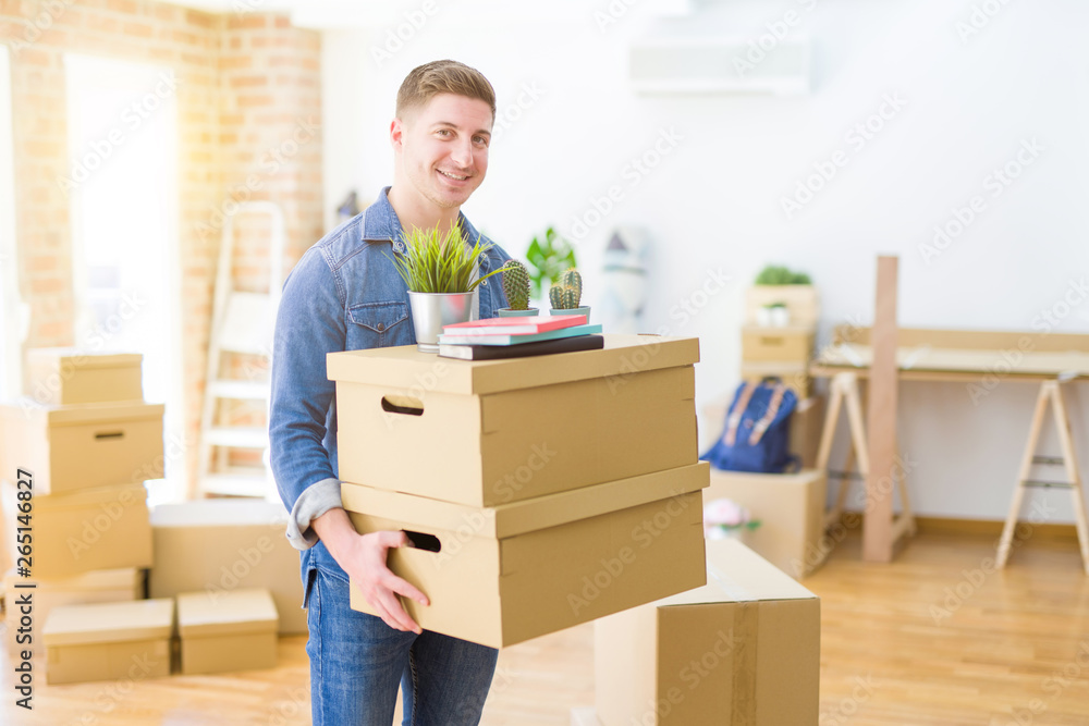 Handsome young man smiling happy moving to a new home, very excited holding cardboard boxes at new apartment Handsome young man smiling happy moving to a new home, very excited holding cardboard boxes at new apartment