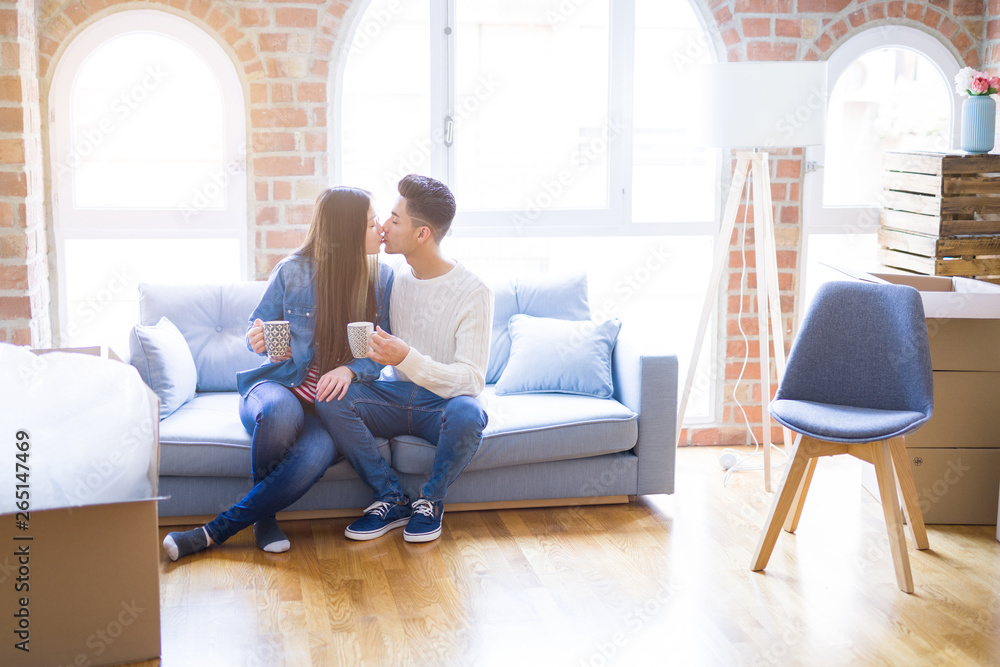 Young asian couple drinking a cup of coffee relaxing on the sofa at new home, smiling happy around cardboard boxes from moving Young asian couple drinking a cup of coffee relaxing on the sofa at new home, smiling happy around cardboard boxes from moving