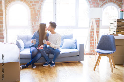 Young asian couple drinking a cup of coffee relaxing on the sofa at new home, smiling happy around cardboard boxes from moving