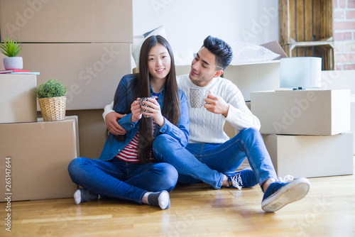 Young asian couple sitting on the floor of new house arround cardboard boxes relaxing from moving drinking a cup of coffe