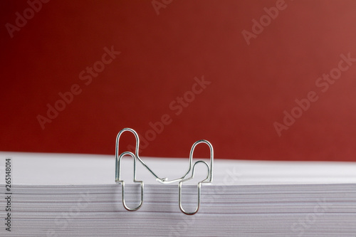 Paper Clips Holding Hands on Paper Pile on Red Background